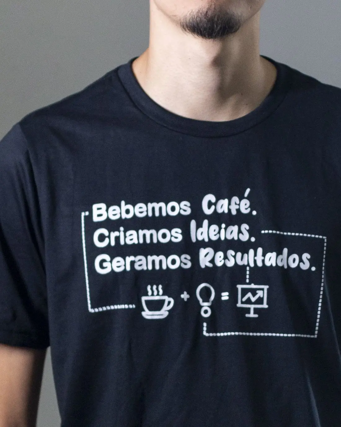 Detalhe da camiseta da equipe com a frase “Bebemos café. Criamos ideias. Geramos resultados.” e os ícones de café, lâmpada e gráfico